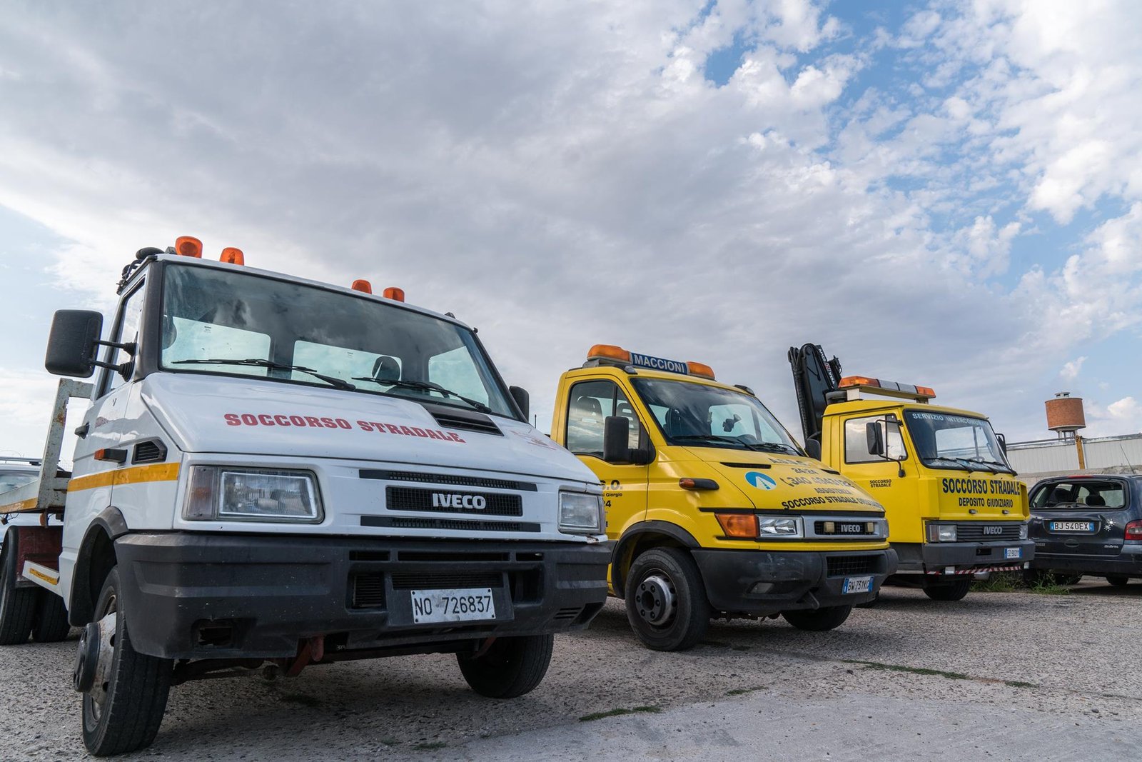 Tre carroattrezzi Iveco, uno bianco e due gialli con scritta Soccorso Stradale, parcheggiati su piazzale sterrato
