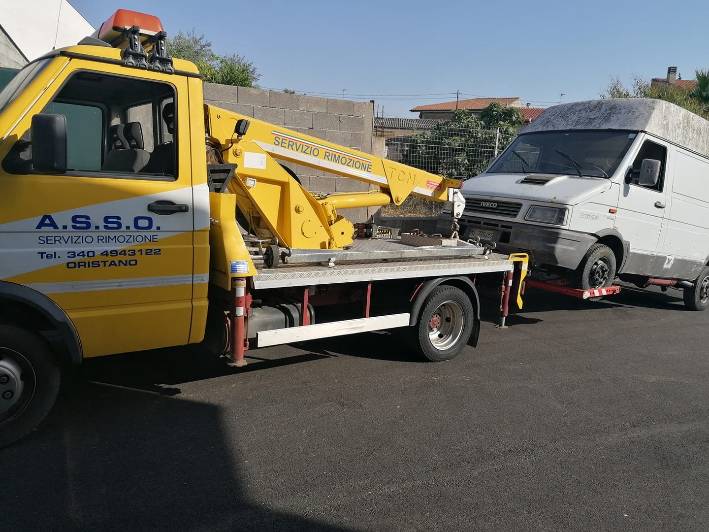 Carro attrezzi giallo A.S.S.O. «Servizio Rimozione» con gru che aggancia un furgone Iveco bianco su asfalto