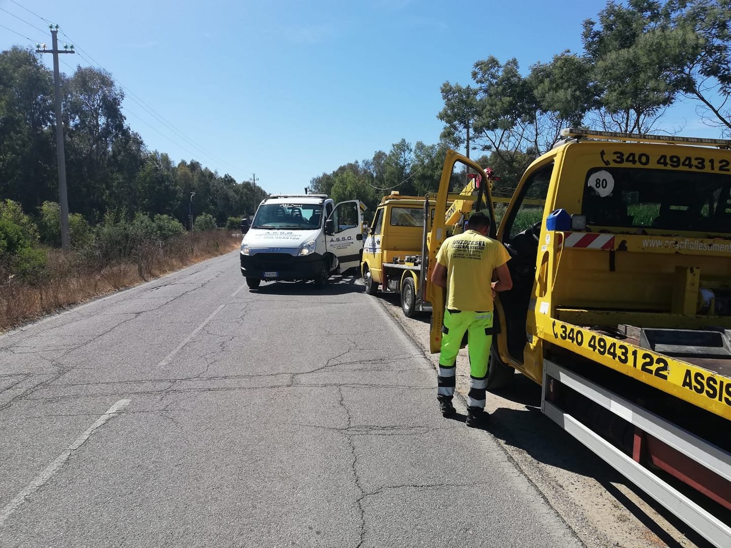 Carroattrezzi gialli A.S.S.O. con numero 340 4943122 e operatore in pantaloni verde fluo su strada di campagna alberata