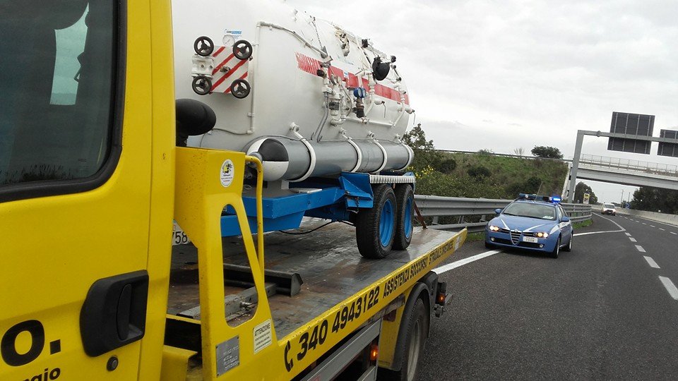 Carroattrezzi giallo A.S.S.O. con cisterna bianca caricata, scritta 340 4943122 e auto della Polizia su superstrada